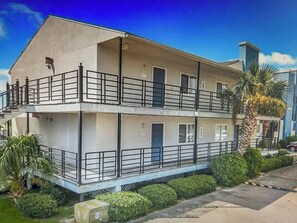 Un edificio de dos pisos con balcones, techo plano y un pequeño jardín.