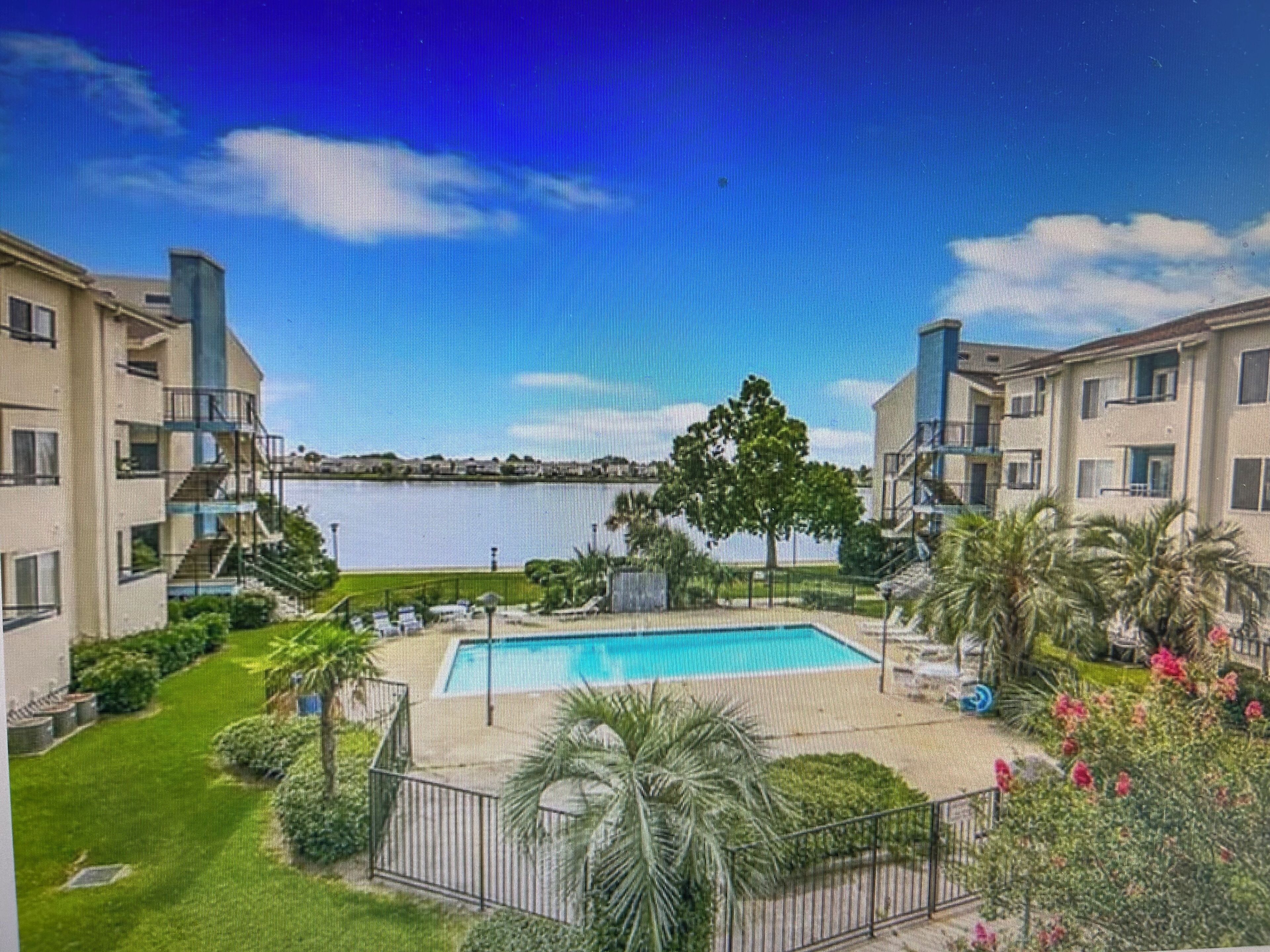 A residential building with a swimming pool, a view of a body of water, and a clear sky.