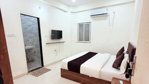 Une chambre à coucher comprenant un lit, un téléviseur, un appareil de climatisation et une porte donnant sur une salle de bain.