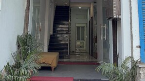 L’entrée de l’hôtel RS Dream se distingue par sa façade en verre transparent, un escalier apparent menant à l’entrée et des plantes en pot disposées à sa base.