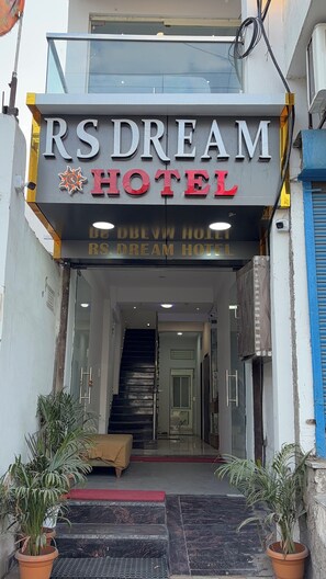 The entrance to RS Dream Hotel with a clear glass facade, a visible staircase leading to the entrance, and potted plants at the base. - RS Dream Hotel (Indore)