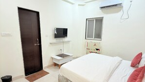 Une chambre avec un lit, une télévision, un petit bureau et un appareil de climatisation.