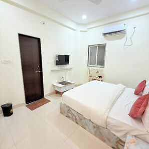 A bedroom with a bed, a TV, a small desk, and an air conditioning unit. - RS Dream Hotel (Indore)
