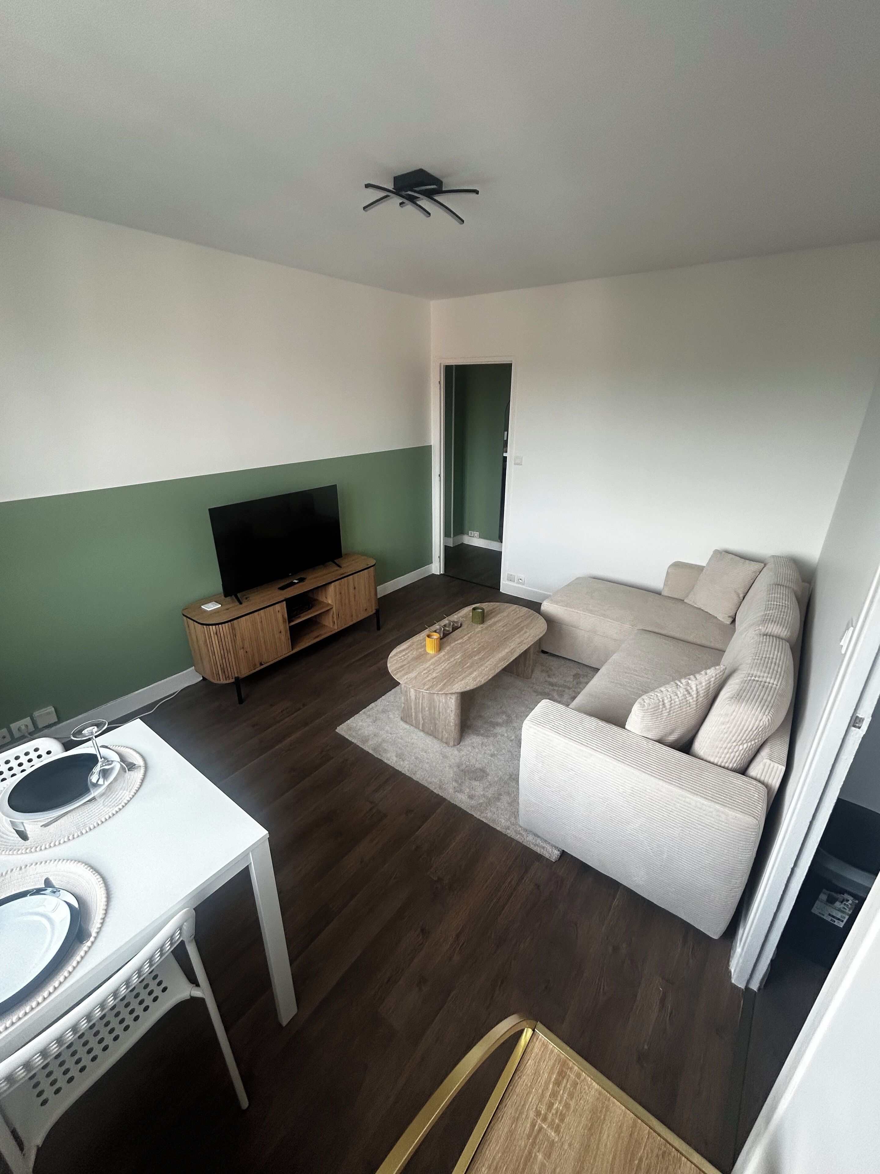 Ein Wohnzimmer mit einer Couch, einem Couchtisch, einem Fernseher auf einem Standfuß, einem Esstisch mit Untertasse und einem Stuhl.