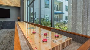 Ein modernes Innenambiente mit einem Kicker, großen Fenstern und Blick auf ein Gebäude.
