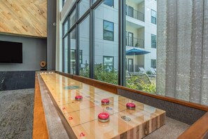 A modern indoor setting with a foosball table, large windows, and a view of a building outside. - Luxury Studio Walk to NRG & Med Center / Pool + Gym (Houston)