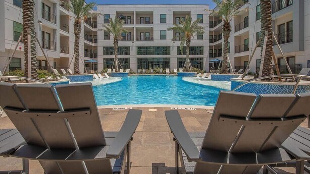 Ein Poolbereich mit Liegestühlen, Palmen und einem Gebäude mit mehreren Balkonen.