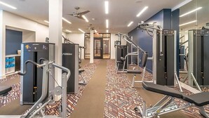 Ein Fitnessstudio mit verschiedenen Trainingsgeräten, einem gemusterten Teppich und einem Deckenventilator.