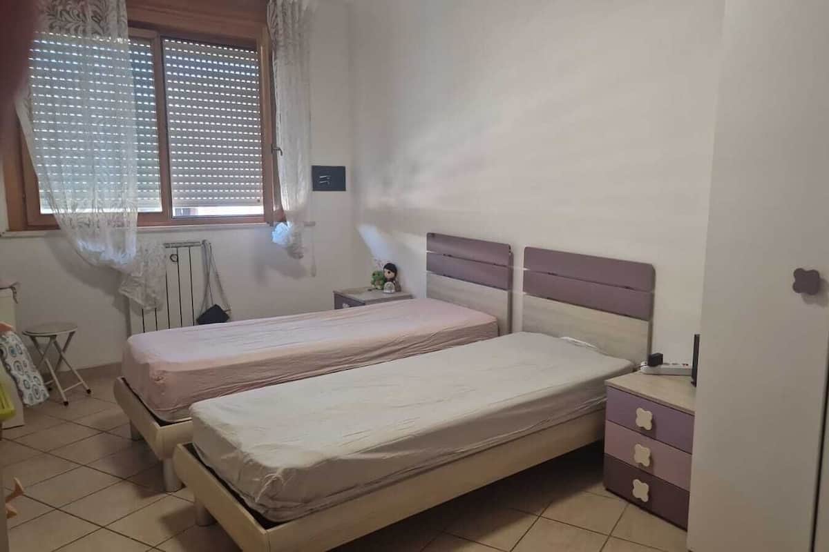 A bedroom with two beds, a nightstand, a wardrobe, and a window with blinds.