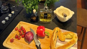 A kitchen counter with a cutting board, knife, tomatoes, red onion, red bell pepper, a loaf of bread, a bottle of oil, and a mortar and pestle. - Le Mas des 3 Frères - sea view - 200m walk to the beach - Domaine de l'Escalet (Ramatuelle)