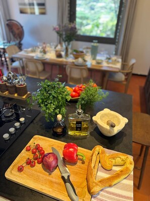 Eine Küchenarbeitsplatte mit Schneidebrett, Messer, Tomaten, roter Zwiebel, roter Paprika, einem Brotlaib, einer Ölflasche und einem Mörser mit Stößel.