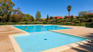 Una piscina rectangular amb un solàrium enrajolat, envoltada per una tanca verda i arbres.