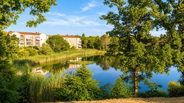 Una vista serena d'un llac amb un edifici de diversos pisos al fons.