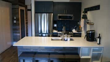 A modern kitchen with dark cabinetry, stainless steel appliances, a white island, and bar seating.