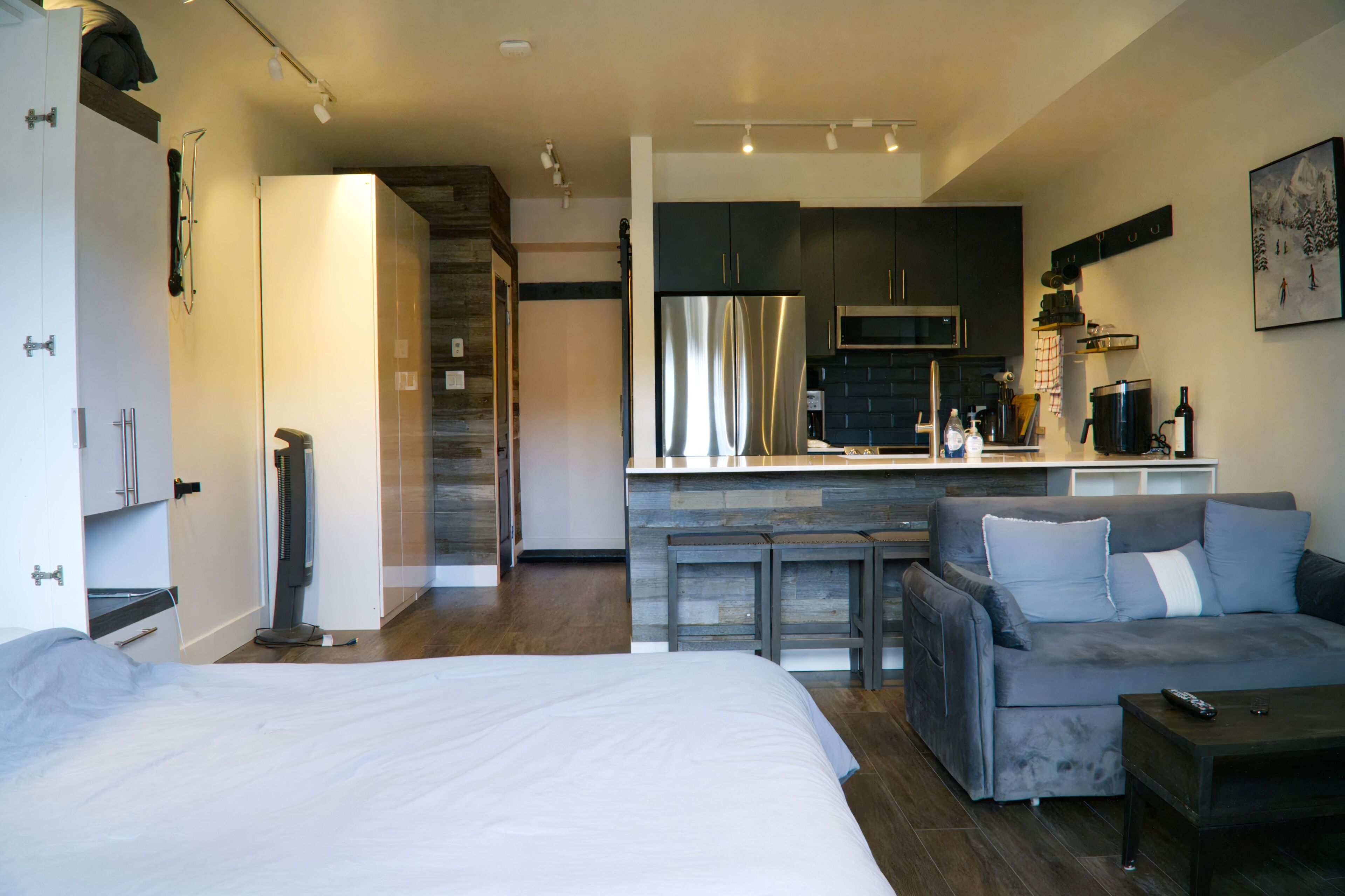 A modern apartment with a large bed, a sofa, a kitchen with a refrigerator, and a dining area.