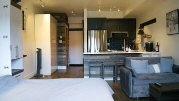 A modern apartment with a large bed, a sofa, a kitchen with a refrigerator, and a dining area.