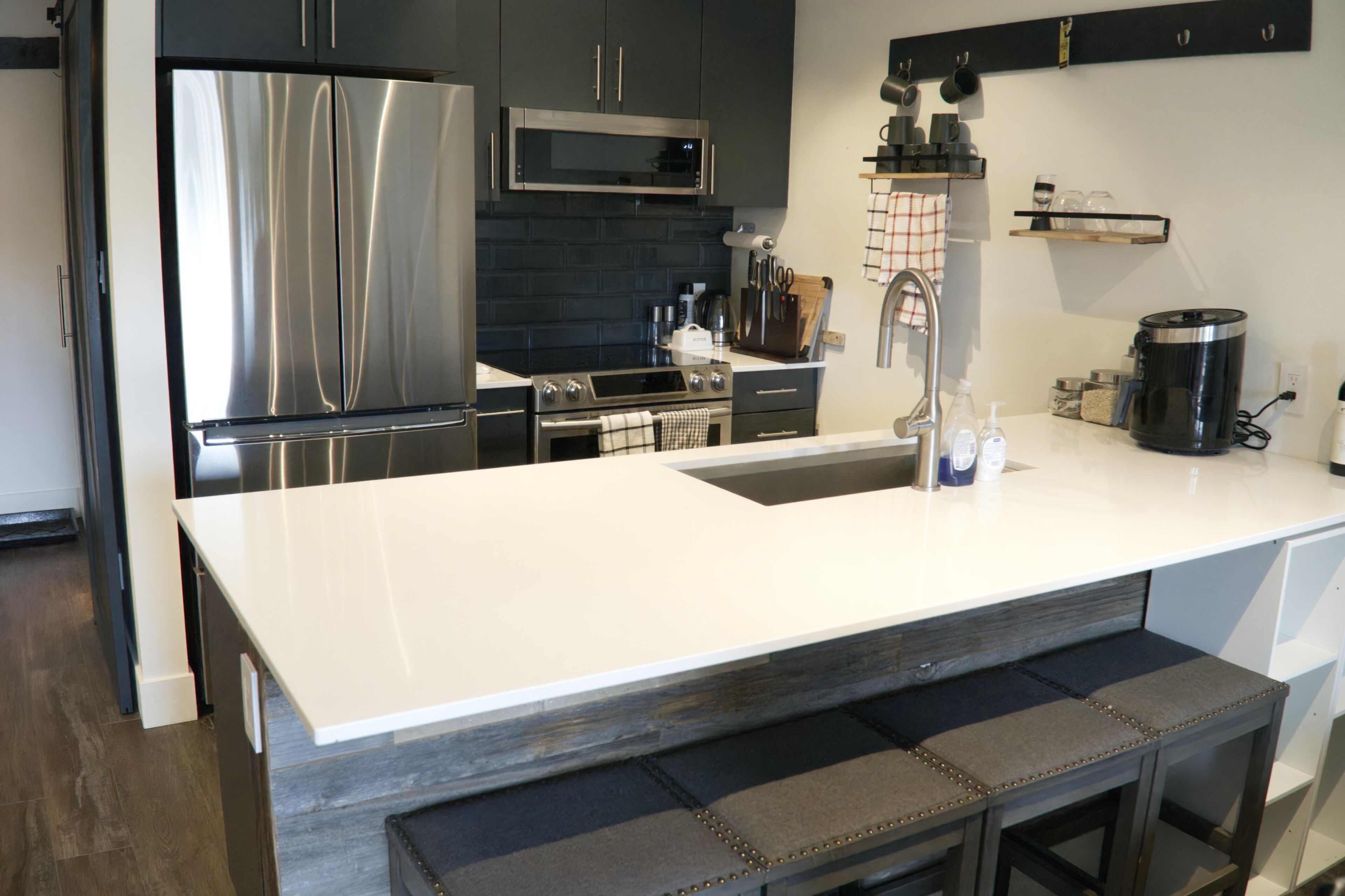 A modern kitchen with stainless steel appliances, a white countertop, and a bar stool.