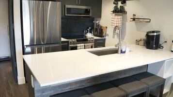 A modern kitchen with stainless steel appliances, a white countertop, and a bar stool.