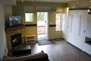 Ein Wohnzimmer mit Kamin aus Stein, Fernseher, einer hölzernen Bank und einer Schiebetür, die auf einen Balkon führt.