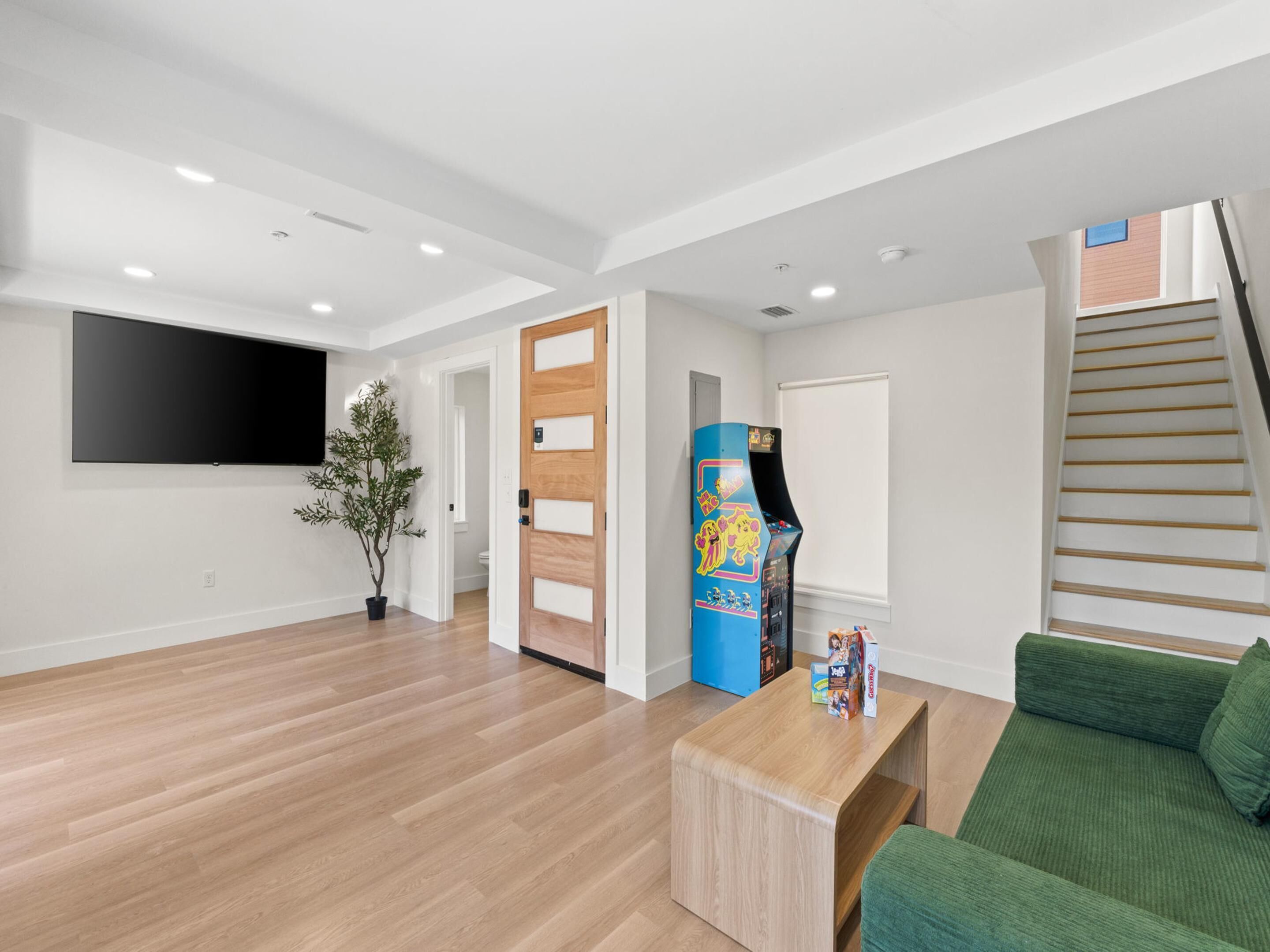 A modern living room with a flat-screen TV, a wooden coffee table, a green sofa, a staircase, and a door leading to another room.