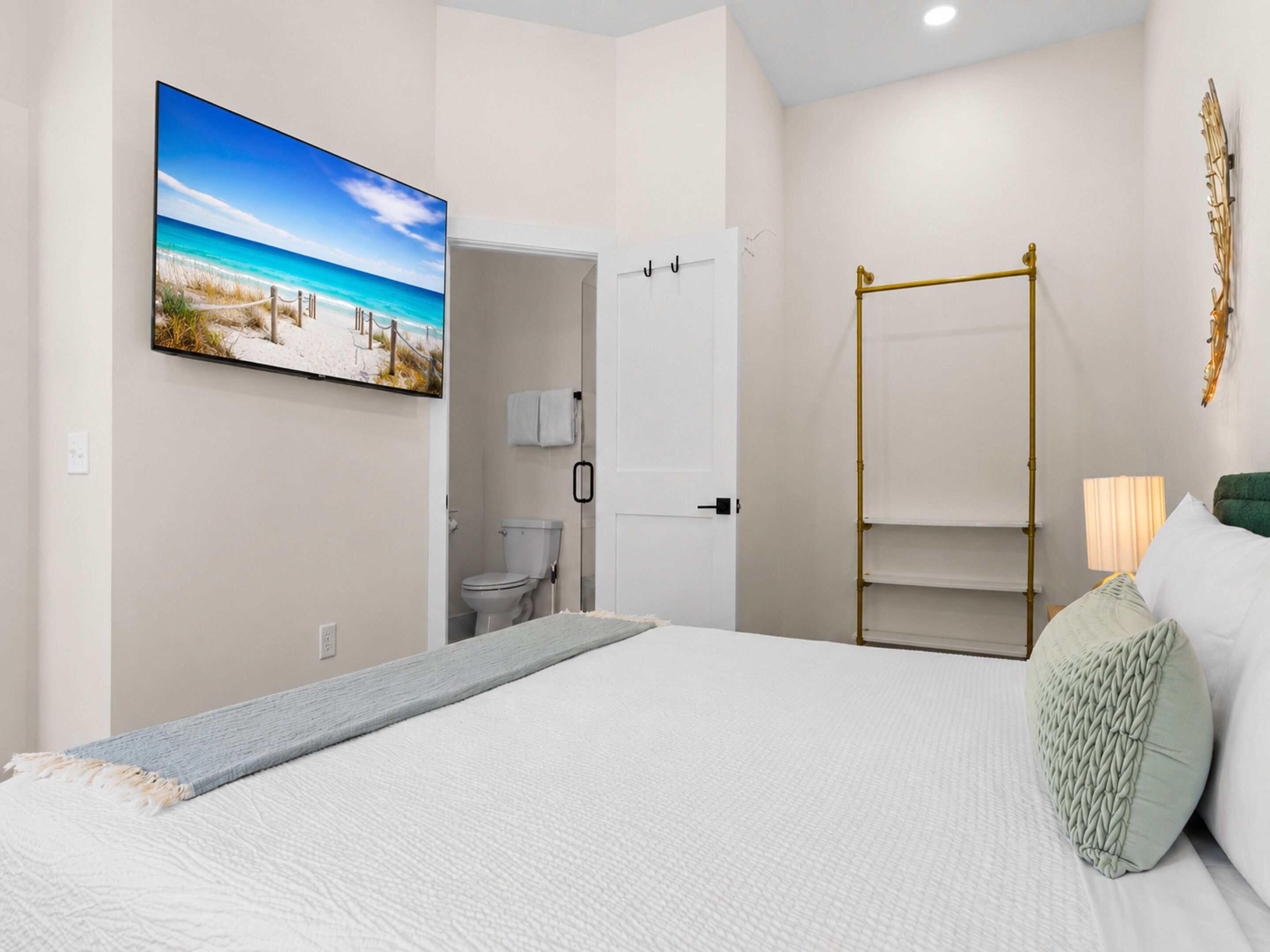 A bedroom with a bed, a painting of a beach, a bathroom, and a wardrobe.