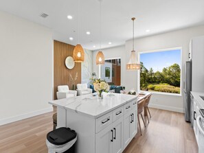 A modern kitchen with a large island, pendant lights, and a view of greenery. - 3006 Emerald Coast C (Panama City Beach)