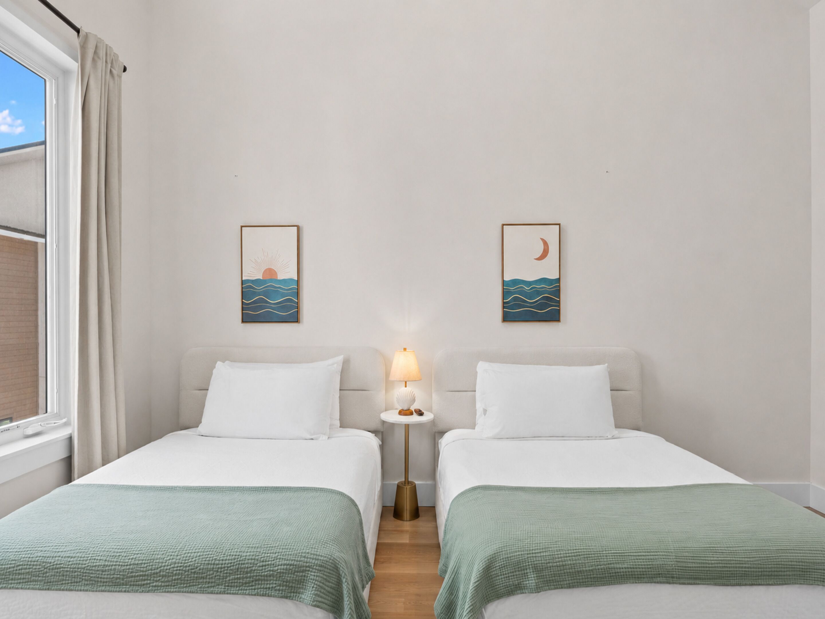A room with two beds, a nightstand with a lamp, and wall art depicting a sun and moon over water.