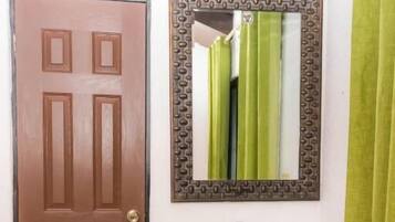 A bathroom with a brown door, a glass sink, a mirror with a patterned frame, and a green curtain.