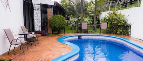 A swimming pool with a curved edge, surrounded by a patio with chairs and a table.