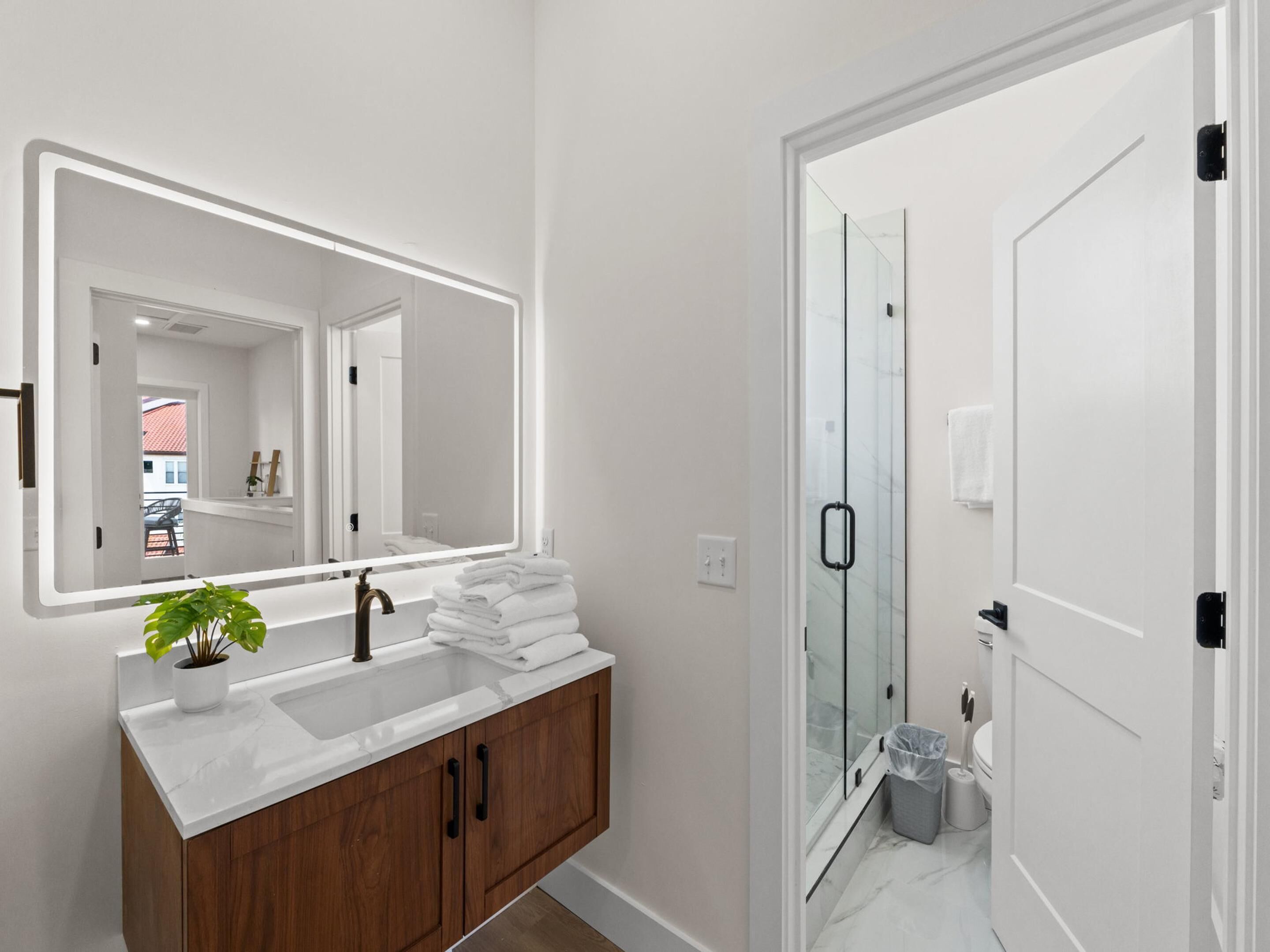 Une salle de bain moderne avec un grand miroir, un lavabo blanc, un meuble-lavabo en bois et une cabine de douche en verre.