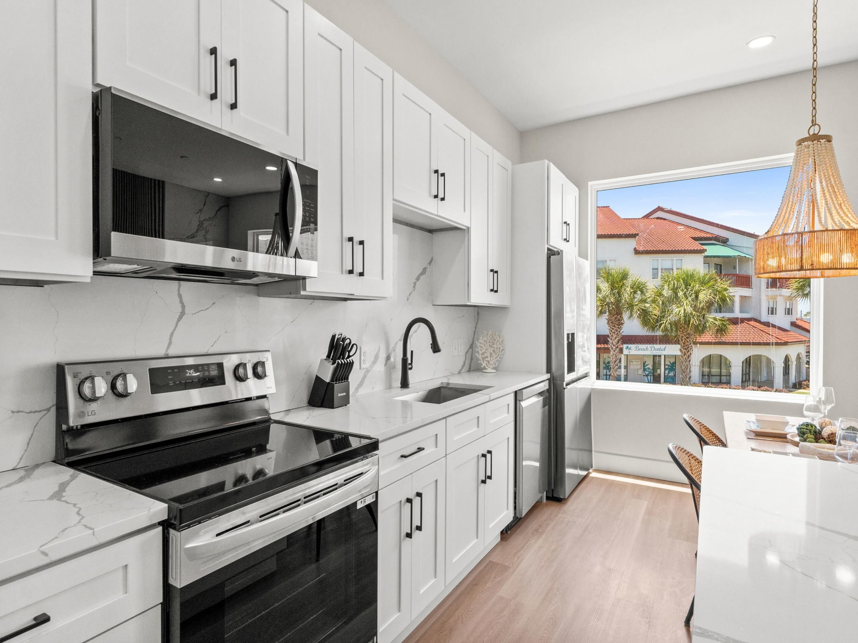 A modern kitchen with white cabinetry, a built-in oven, a sink, and a window with a view of buildings.