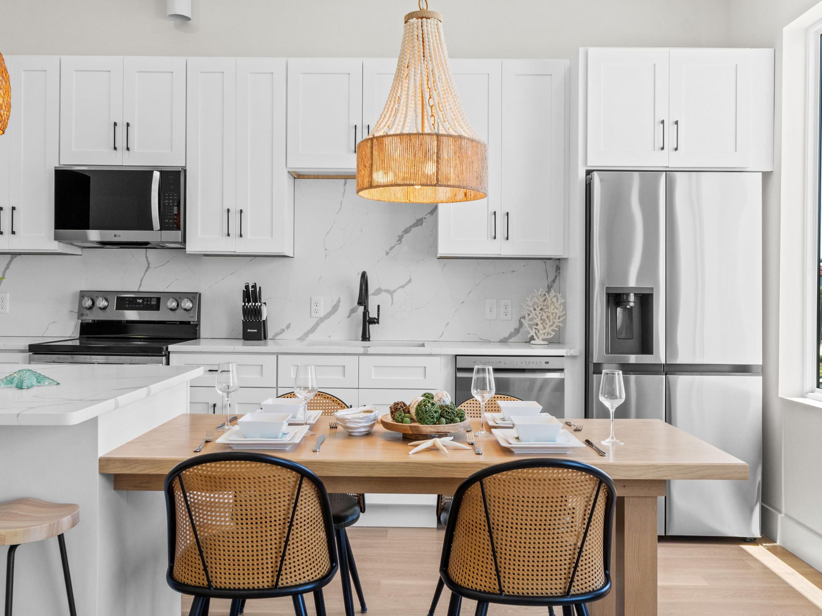 A modern kitchen with white cabinets, stainless steel appliances, a central island with seating, and a hanging light fixture.