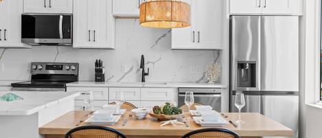 A modern kitchen with white cabinets, stainless steel appliances, a central island with seating, and a hanging light fixture.