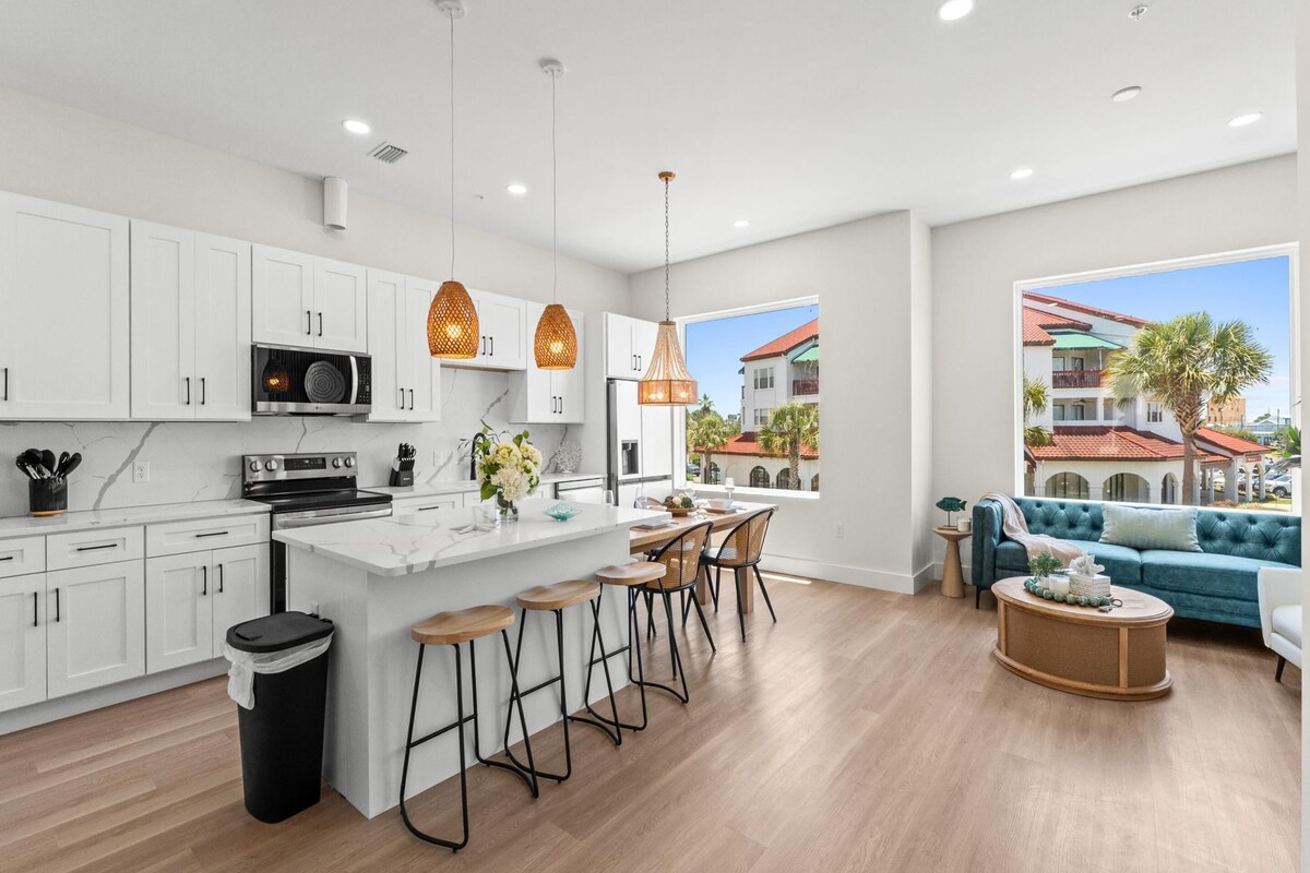 A modern kitchen with white cabinets, a central island, bar stools, and pendant lighting.