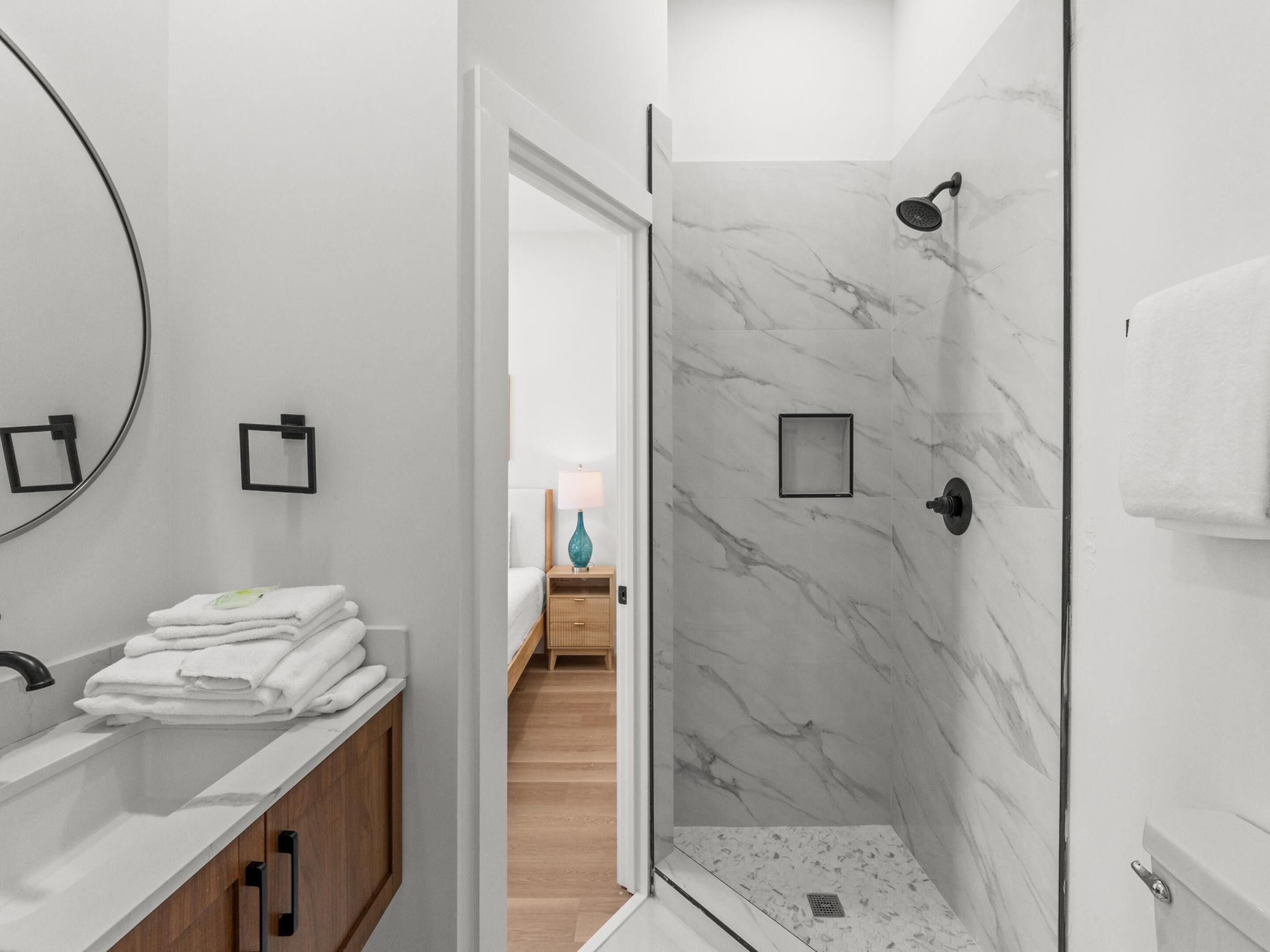 A modern bathroom with a shower, a sink with a mirror, and a stack of towels.
