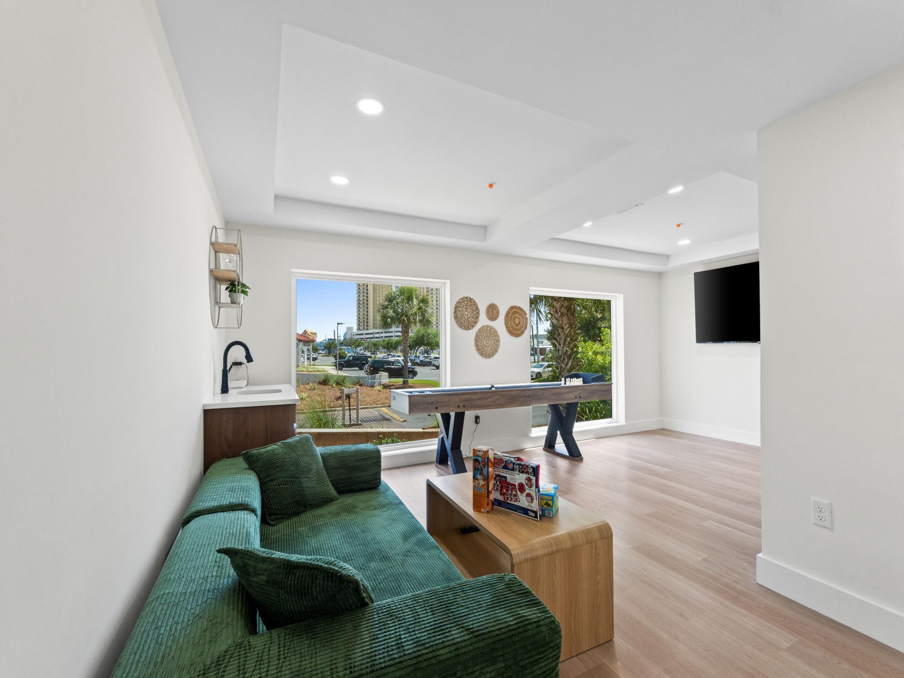 A modern living room with a green sofa, a pool table, and a view of a cityscape through large windows.