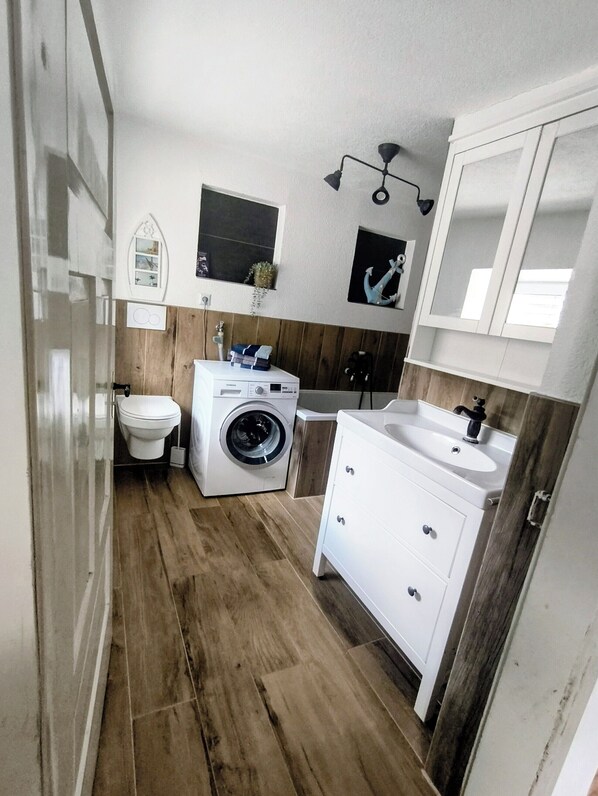 A compact bathroom with a washing machine, a toilet, a sink, and a mirror.