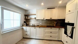 A kitchen with white cabinets, a wooden countertop, a window, and a pink rug. - Vacation cottage Obermarchtal (Obermarchtal)
