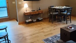 A dining area with a table, chairs, a TV mounted on the wall, and a wooden floor. - The Farm House at Bliss Point Ranch FM-17 (Grand Saline)