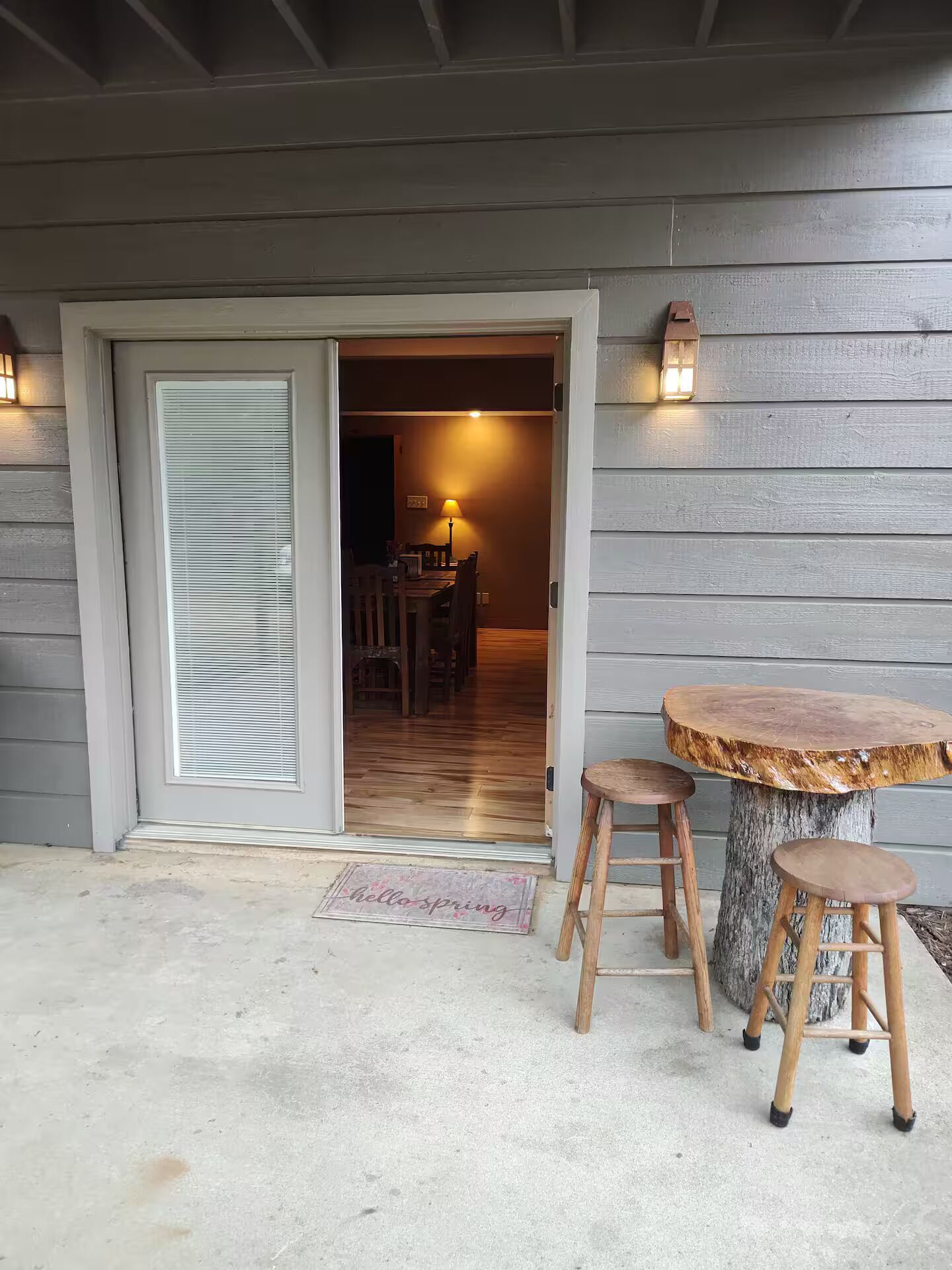 Een inkom met een schuifdeur van glas, een ronde houten tafel met krukken, en twee wandlampen.