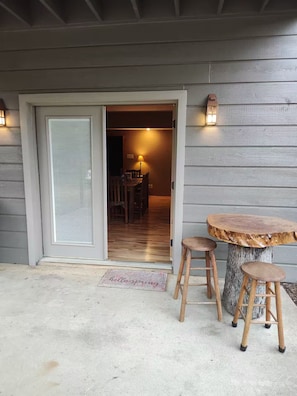 Une entrée avec une porte coulissante en verre, une table ronde en bois entourée de tabourets et deux lanternes fixées au mur.