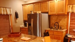 A kitchen with wooden cabinets, a granite countertop island, a stainless steel refrigerator, and a sink. - The Farm House at Bliss Point Ranch FM-17 (Grand Saline)