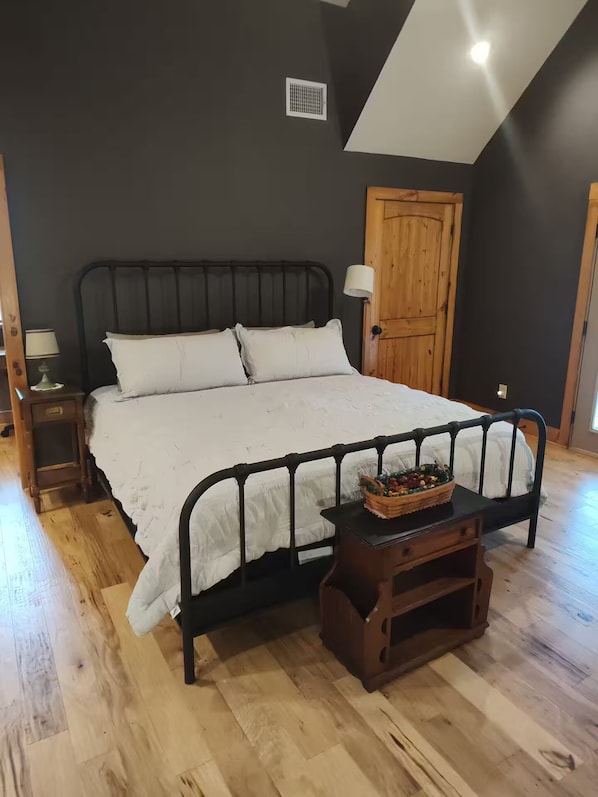 Une chambre à coucher avec un lit, une table de chevet, une porte en bois et une petite table sur laquelle se trouve un panier.