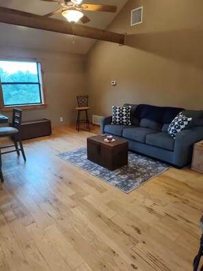 Un salon comprenant un canapé, une table basse en bois, un fauteuil, une fenêtre et un ventilateur de plafond.