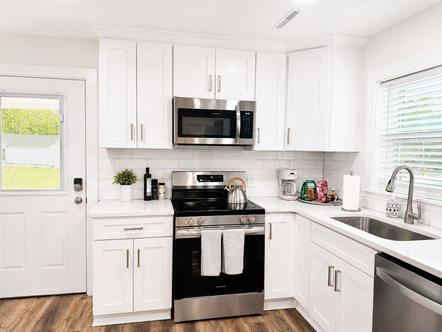 Una cocina moderna con armarios blancos, electrodomésticos de acero inoxidable y piso de madera.