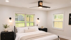 Une chambre à coucher comprenant un lit, deux tables de chevet, un ventilateur de plafond et deux fenêtres.