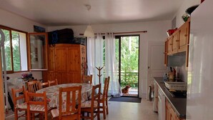 A kitchen with wooden cabinets, a dining table with chairs, a fan, and a view through the door. - The 3 Pignons gourmet refuge (Noisy-sur-École)