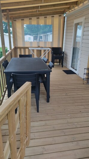 Eine überdachte Terrasse mit Tisch und Stühlen, einem Holzbalkon und Blick auf die Umgebung.
