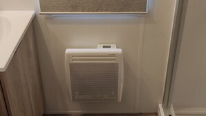 Un baño con ventana, radiador blanco, suelo de madera y alfombra oscura.