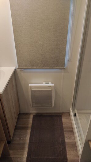 Ein Badezimmer mit Fenster, einem weißen Heizkörper, Holzboden und einem dunklen Teppich.